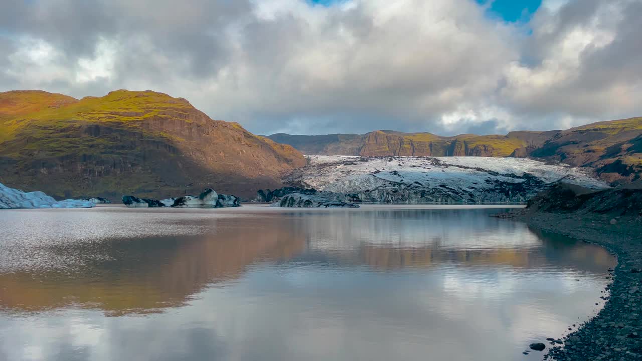 阳光照耀下的Sólheimajökull冰岛冰川反射在宁静的湖泊中，与戏剧性的天空