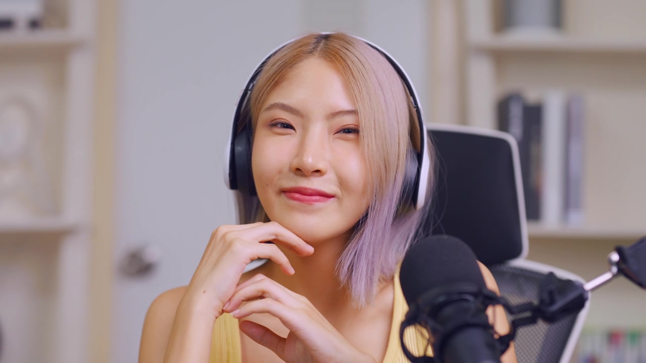 詳情圖-亞洲音頻DJ女士對(duì)著麥克風(fēng)講話的肖像。迷人美麗的女性博主影響者戴著耳機(jī)，在家庭工作室為電臺(tái)錄制早間新聞播客節(jié)目。