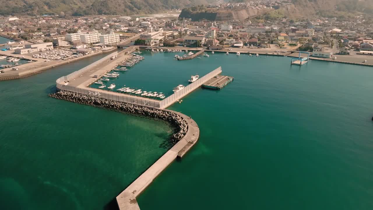 蔚蓝的大海和一个小渔港的堤岸鸟瞰图，在一个阳光明媚的日子里，渔船停泊在那里