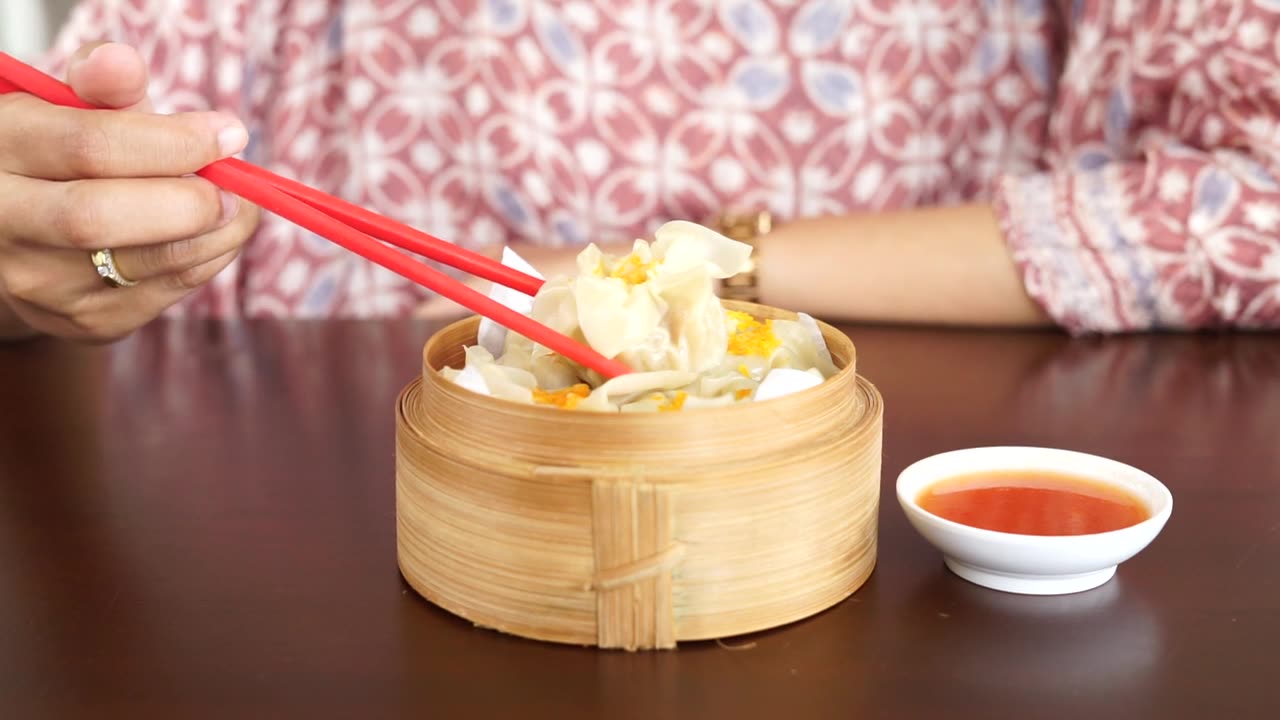 詳情圖-一位婦女正在用紅筷子吃蘸著醬汁的點心餃子