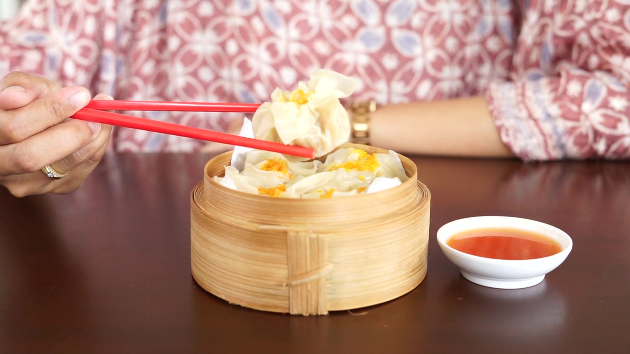 詳情圖-一位婦女正在用紅筷子吃蘸著醬汁的點心餃子