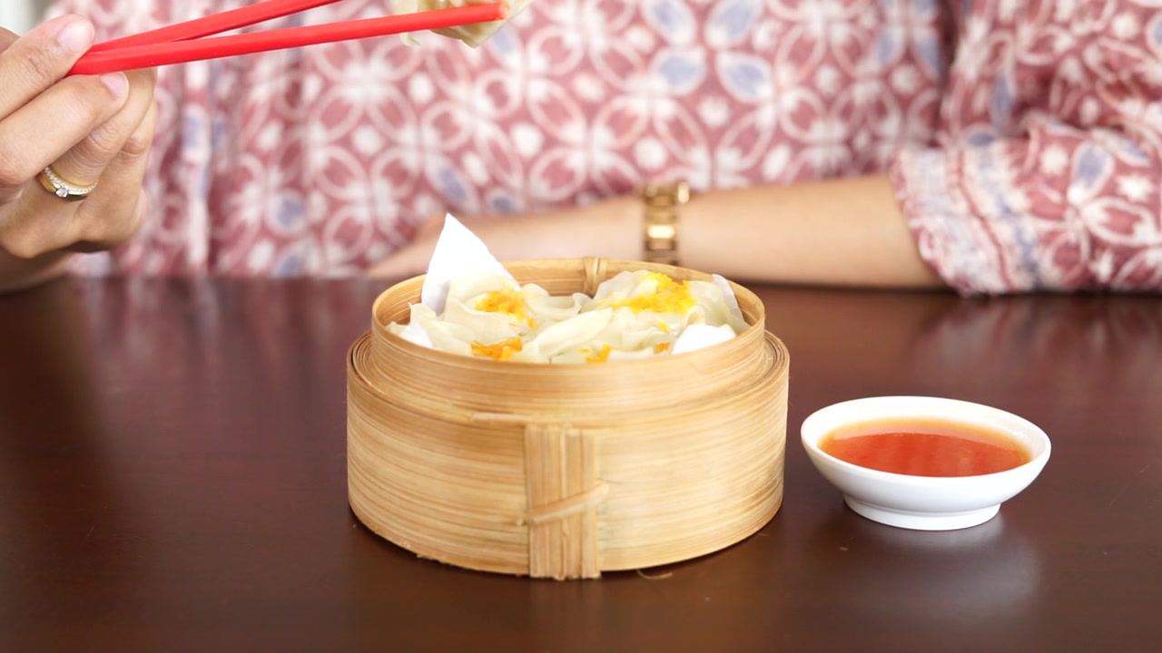 詳情圖-一位婦女正在用紅筷子吃蘸著醬汁的點心餃子