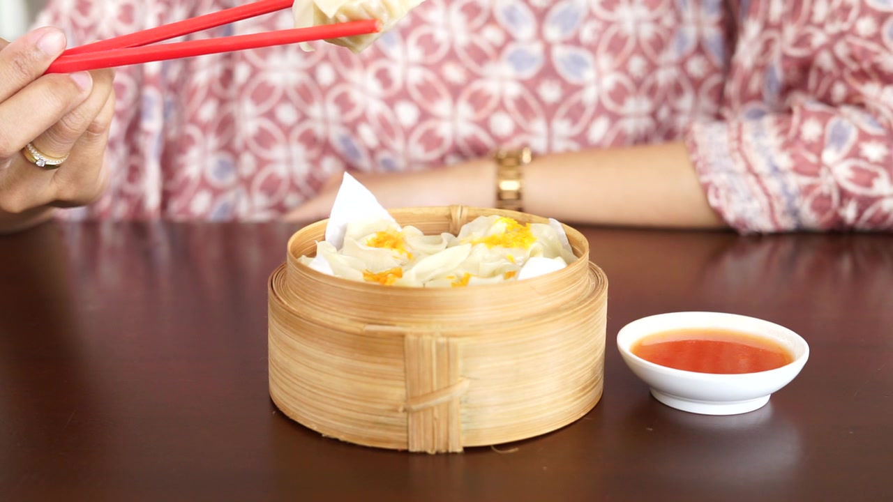 詳情圖-一位婦女正在用紅筷子吃蘸著醬汁的點心餃子