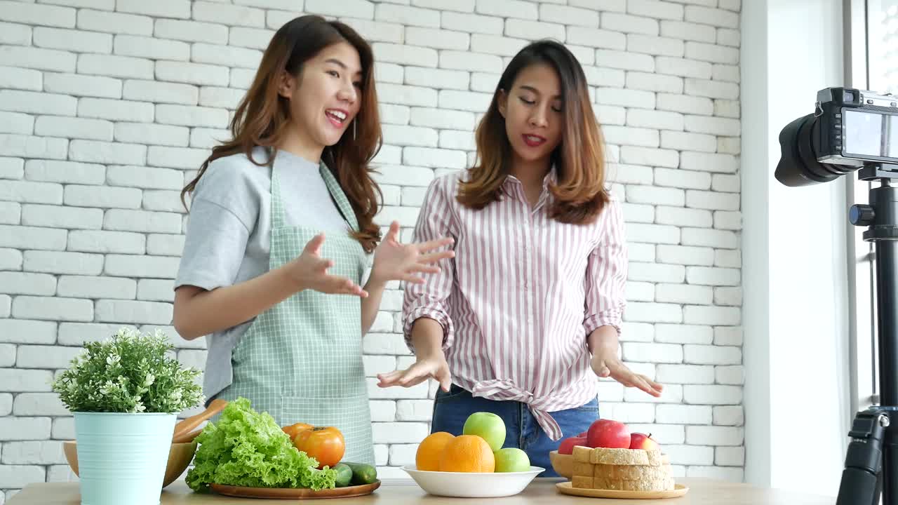 亚洲网红视频博主直播健康饮食生活方式。两个年轻的女性朋友博主vlog快乐的生活方式如何吃蔬菜，水果，素食产品。两个女人在谈论社交媒体视频