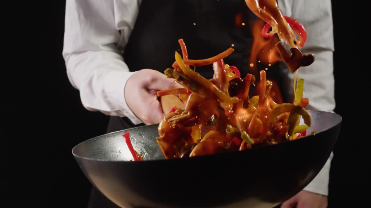 厨师在炒锅上炒菜拌虾特写。对虾着火了，扔到锅里。餐饮概念。海洋食品。