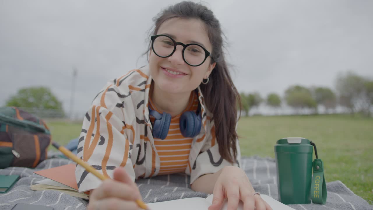 女学生在公园草地上休息，在网络通话中对着摄像机说话