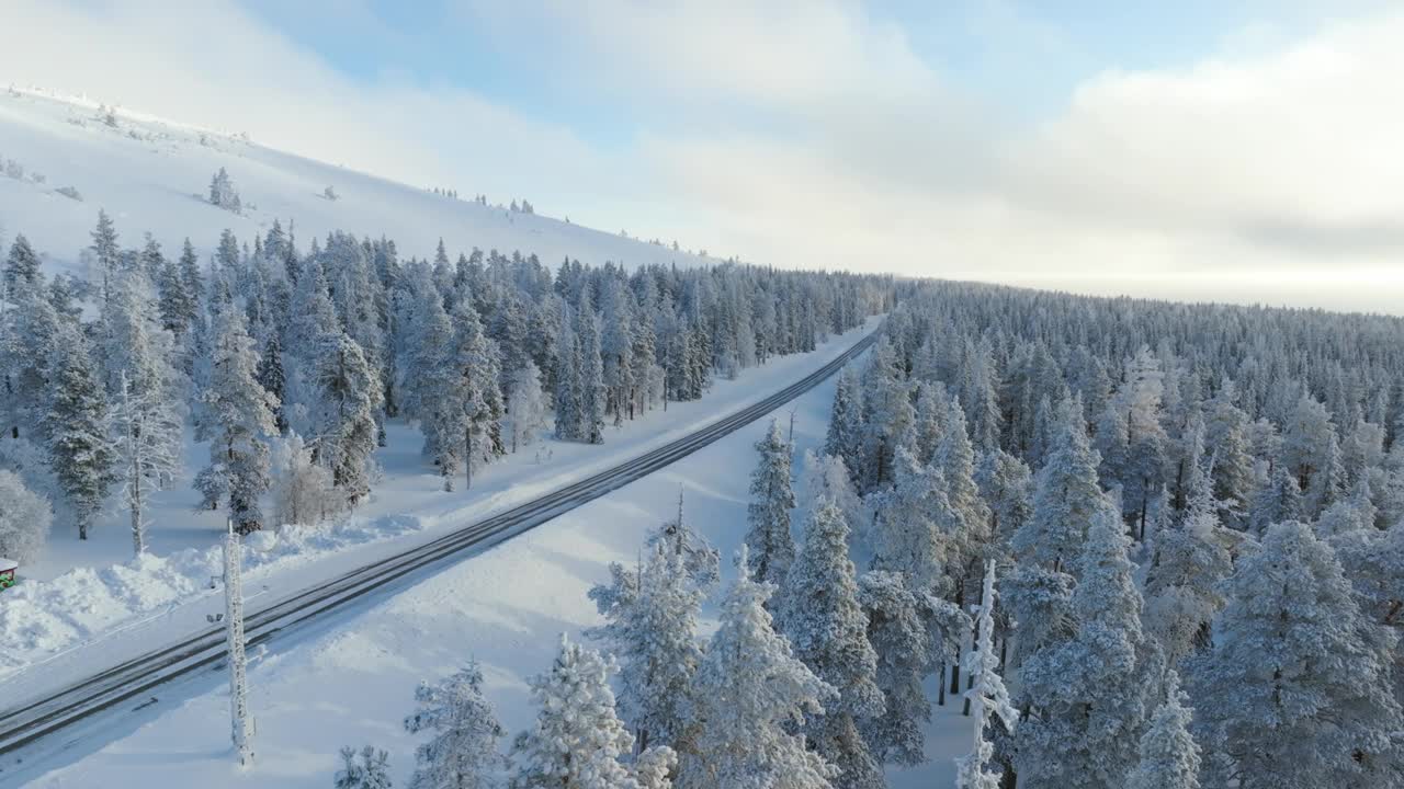 无人机尾随一辆红色电动汽车行驶在冬季拉普兰的雪林中