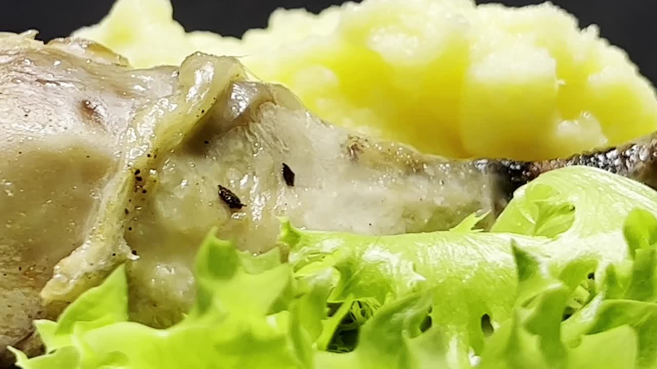 白色盘子里的鸡腿配土豆泥和生菜叶。近距离射击。