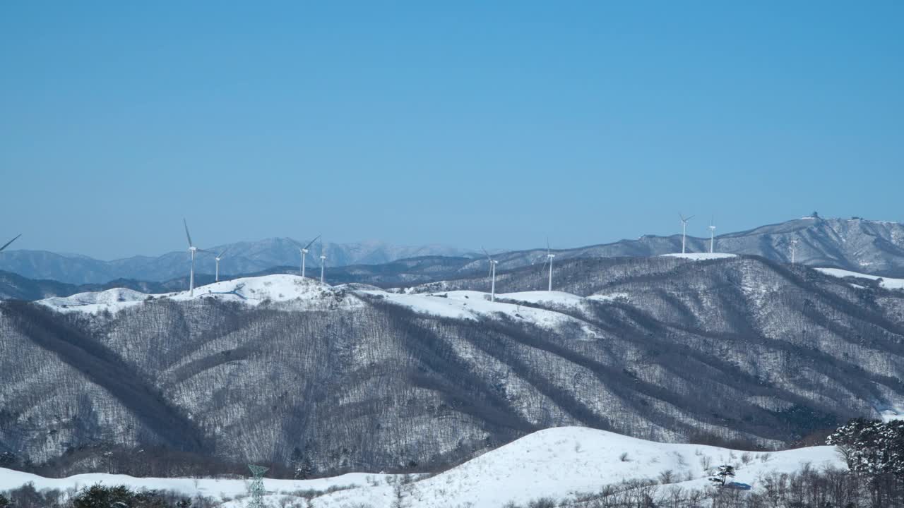 冬天的江原道，在晴朗的霜冻的蓝天下，白雪覆盖的山顶上有风车