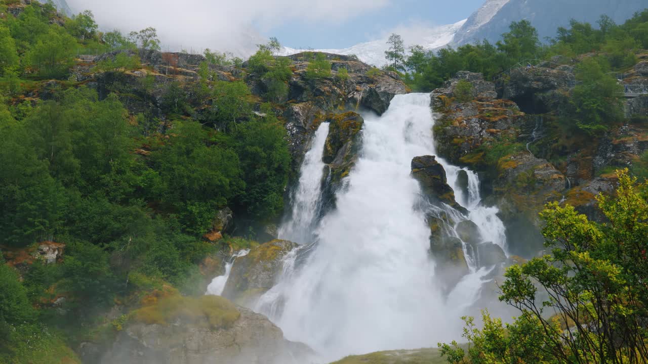 美丽的瀑布从冰川的水。在背景中，山顶有冰的山是布里克斯达尔冰川。挪威和斯堪的纳维亚半岛的自然