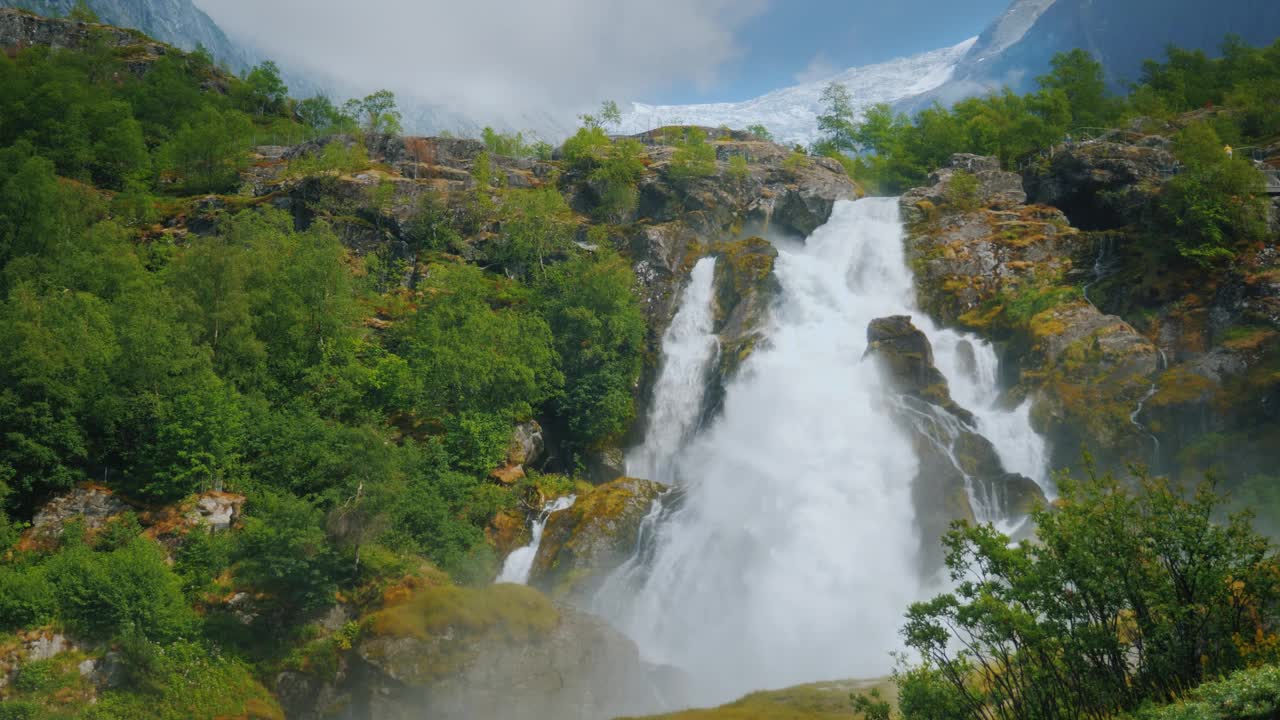 美丽的瀑布从冰川的水。在背景中，山顶有冰的山是布里克斯达尔冰川。挪威和斯堪的纳维亚半岛的自然