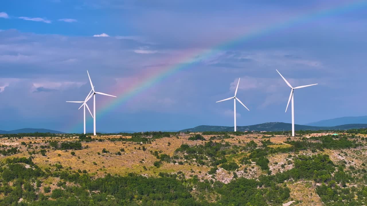 航拍:在崎岖的风景衬托下，风力涡轮机上空出现了一道引人注目的彩虹。