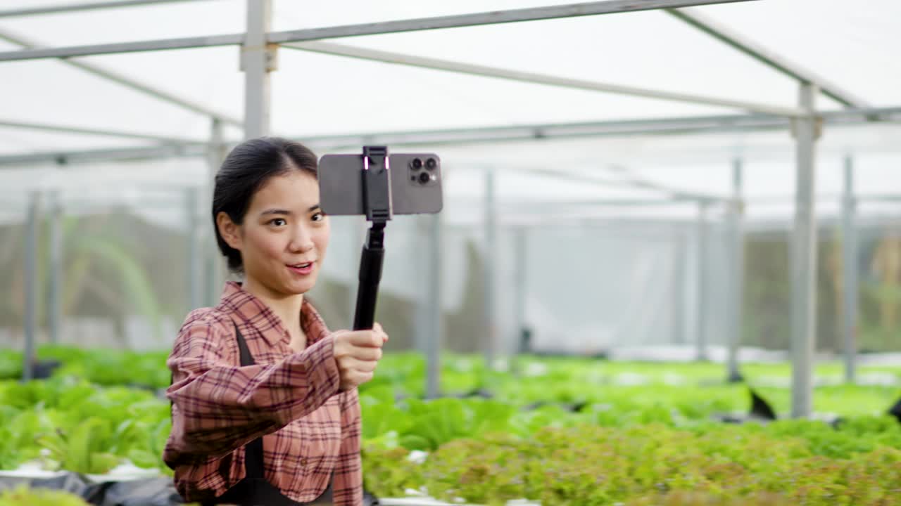 穿着格子衬衫的年轻亚洲女农民的肖像，用智能手机对着视讯流回顾她的有机蔬菜农场，拥有技术设备概念的聪明农民