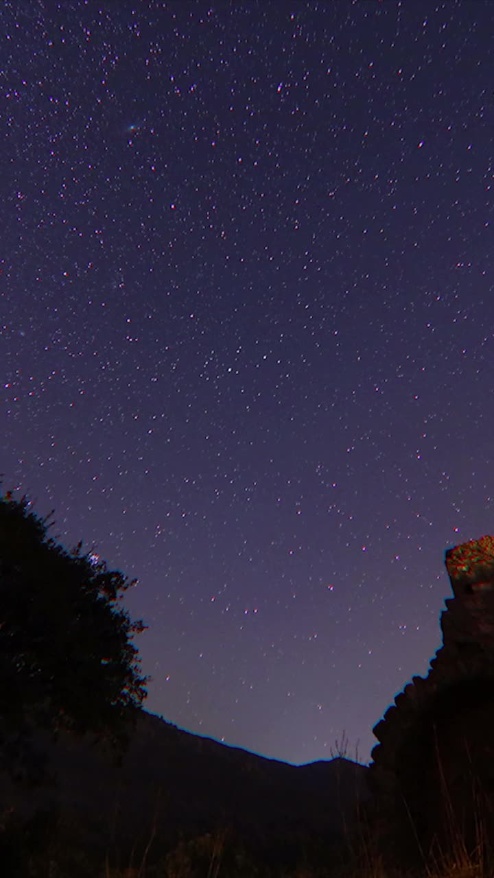 夜晚的古堡。移动的星迹在夜空中的时间间隔。这是一幅银河系恒星的景象，前景中有一座山顶。英仙座流星雨观测。垂直视频。