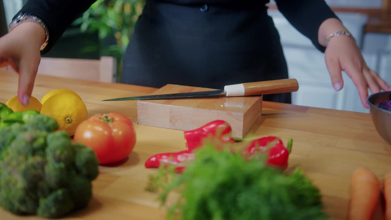 一名妇女用菜刀在砧板上切新鲜的青椒，准备做饭。在家庭厨房里烹饪食物的概念