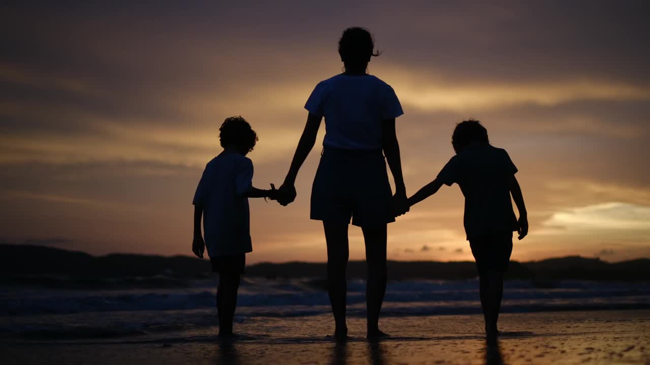 母亲带着两个孩子在海滩上日落剪影家庭度假夏日海滩一起度过美好时光