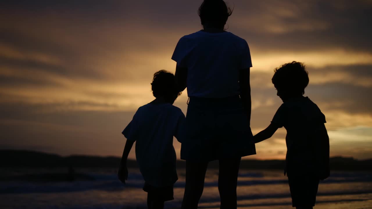 母亲带着两个孩子在海滩上日落剪影家庭度假夏日海滩一起度过美好时光