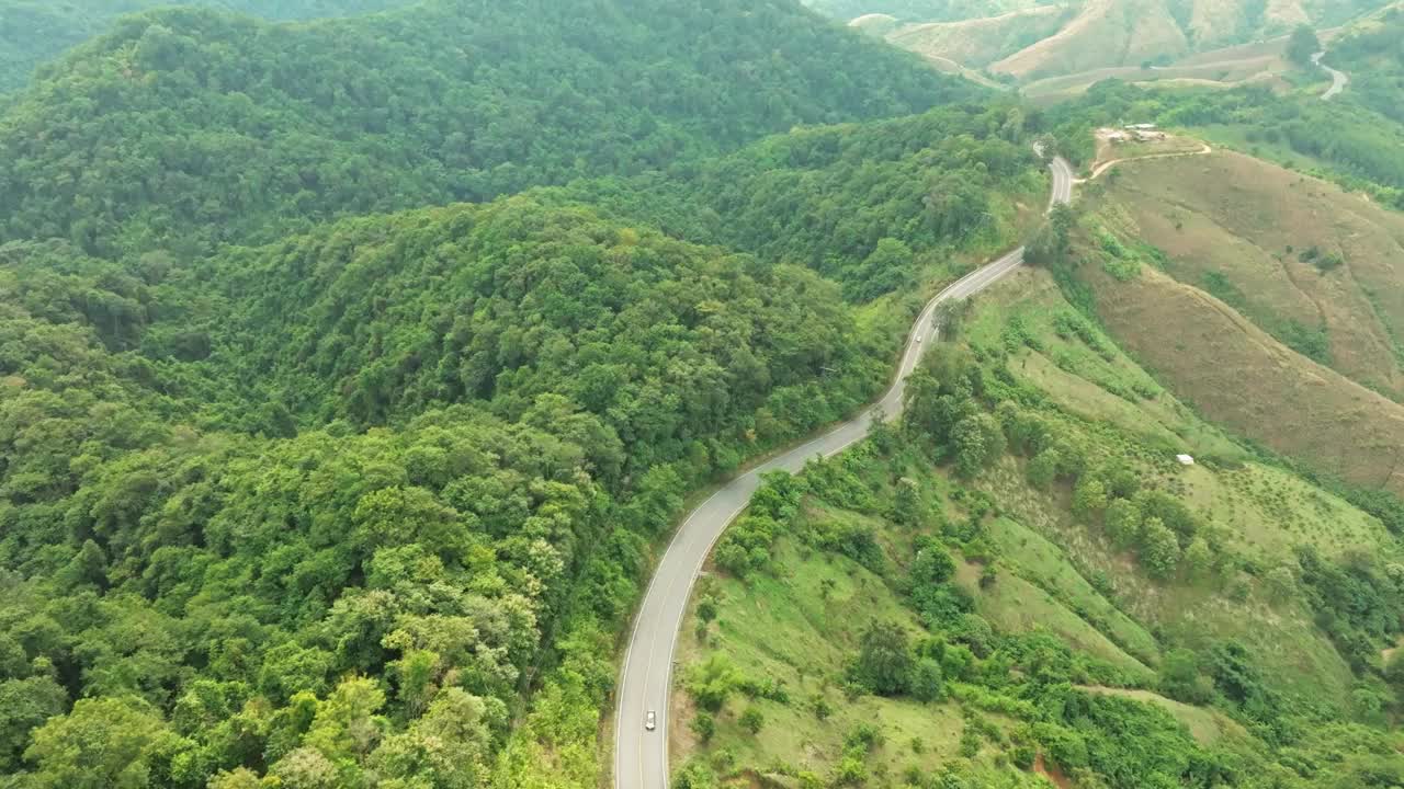 鸟瞰深绿色的森林道路和白色的电动车自然景观和高架道路探险旅行交通和环保理念