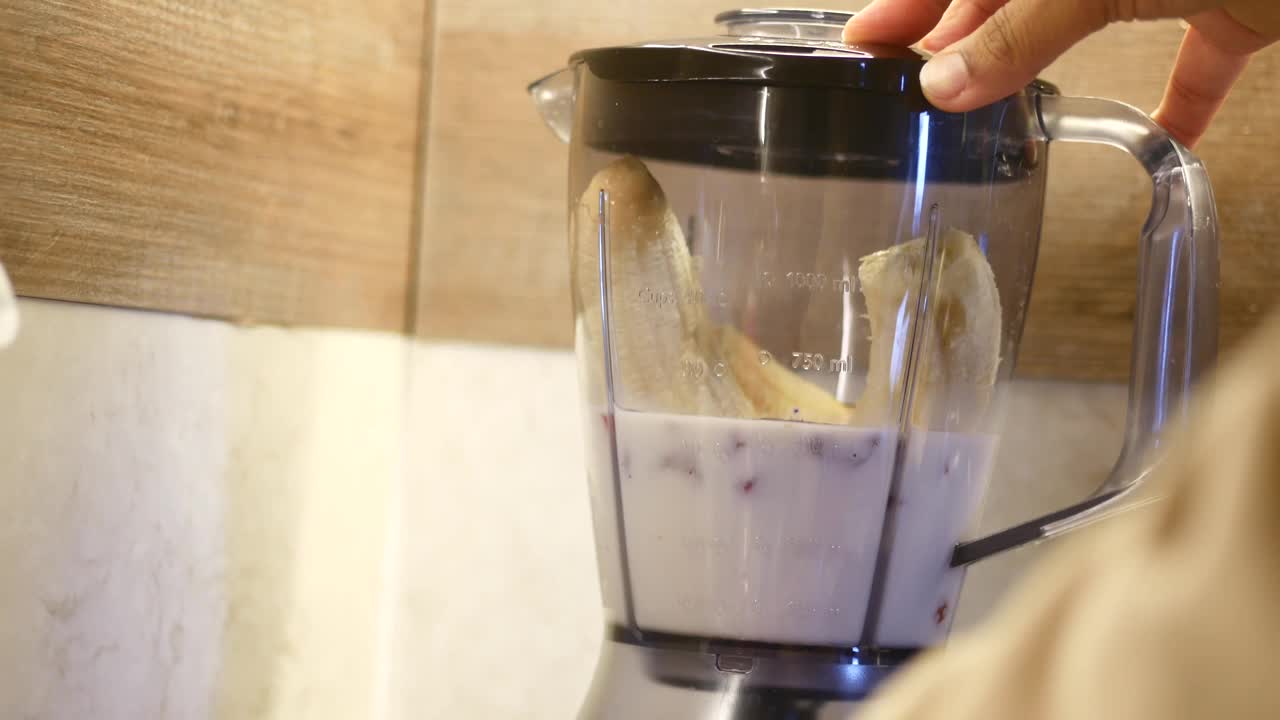用搅拌器与厨房用具中的食物和液体一起制作冰沙的人