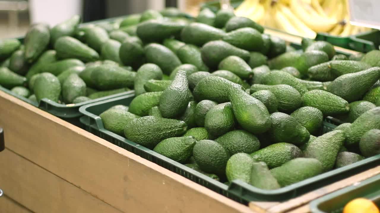 一名买家在超市挑选牛油果。男顾客在杂货店买青菜。健康饮食理念。