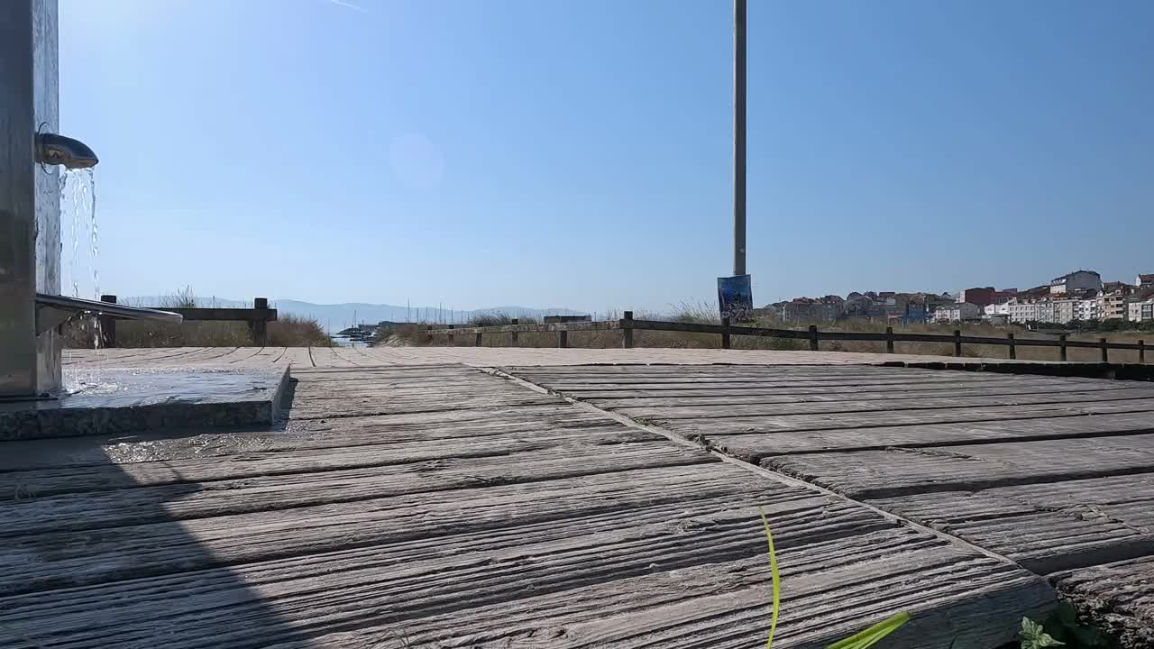 西班牙加利西亚蓬特维德拉，黎明时分，一男一女走在通往大海的古老木制长廊上，喷泉龙头将饮用水泼向干燥的地面，拍摄被阻断