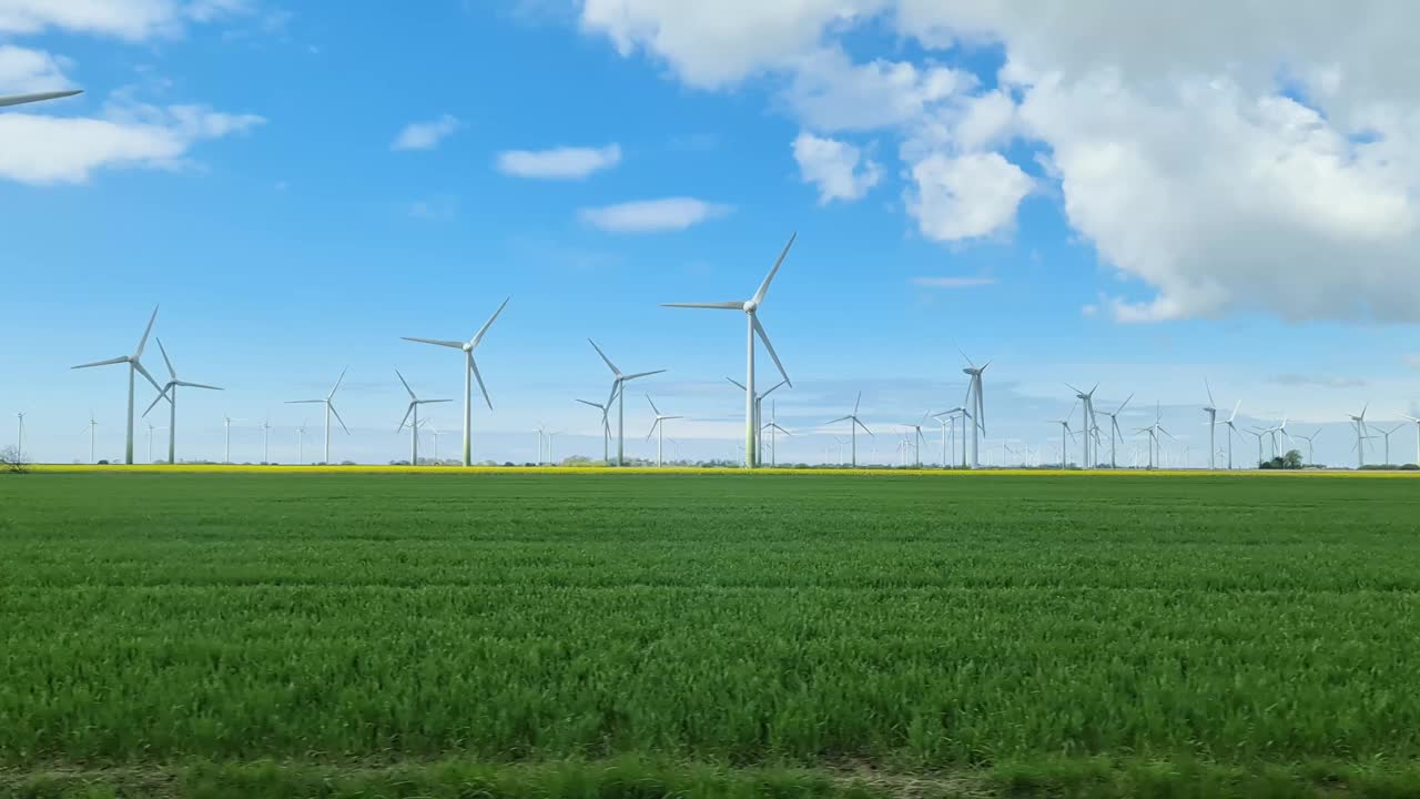 從行駛中的汽車側窗看到草地上的大型風力發(fā)電場。