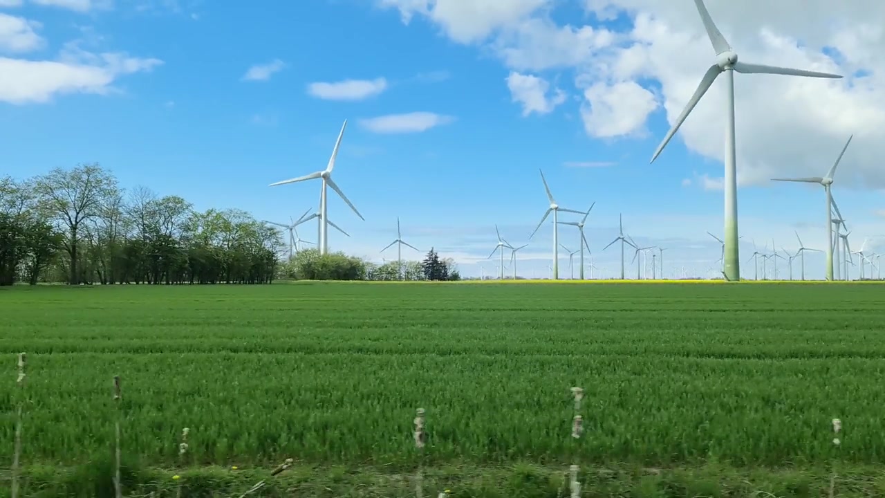 詳情圖-從行駛中的汽車側窗看到草地上的大型風力發(fā)電場。