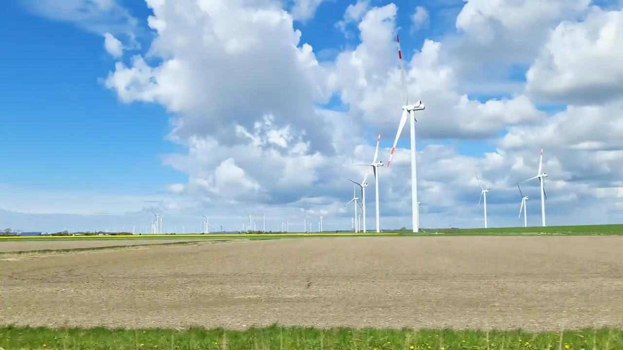 詳情圖-從行駛中的汽車側(cè)窗看到草地上的大型風(fēng)力發(fā)電場(chǎng)。