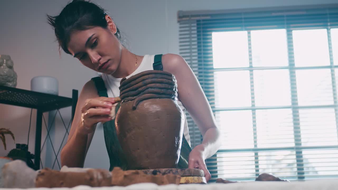 一位女陶艺家正在车间里制作一件新陶器。一位亚洲妇女正在享受陶艺工作。