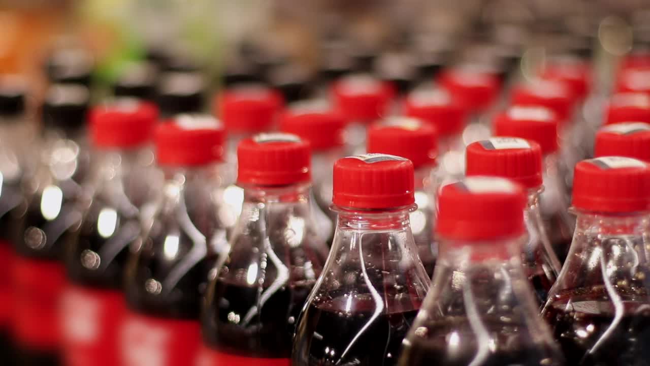高加索女买家手拿一个塑料瓶甜碳酸饮料。女顾客在店里挑选可乐。不健康饮食概念。特写镜头