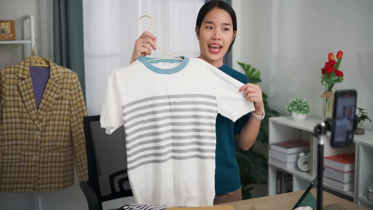 年轻的女企业主站在家里一边卖衣服一边用手机直播。