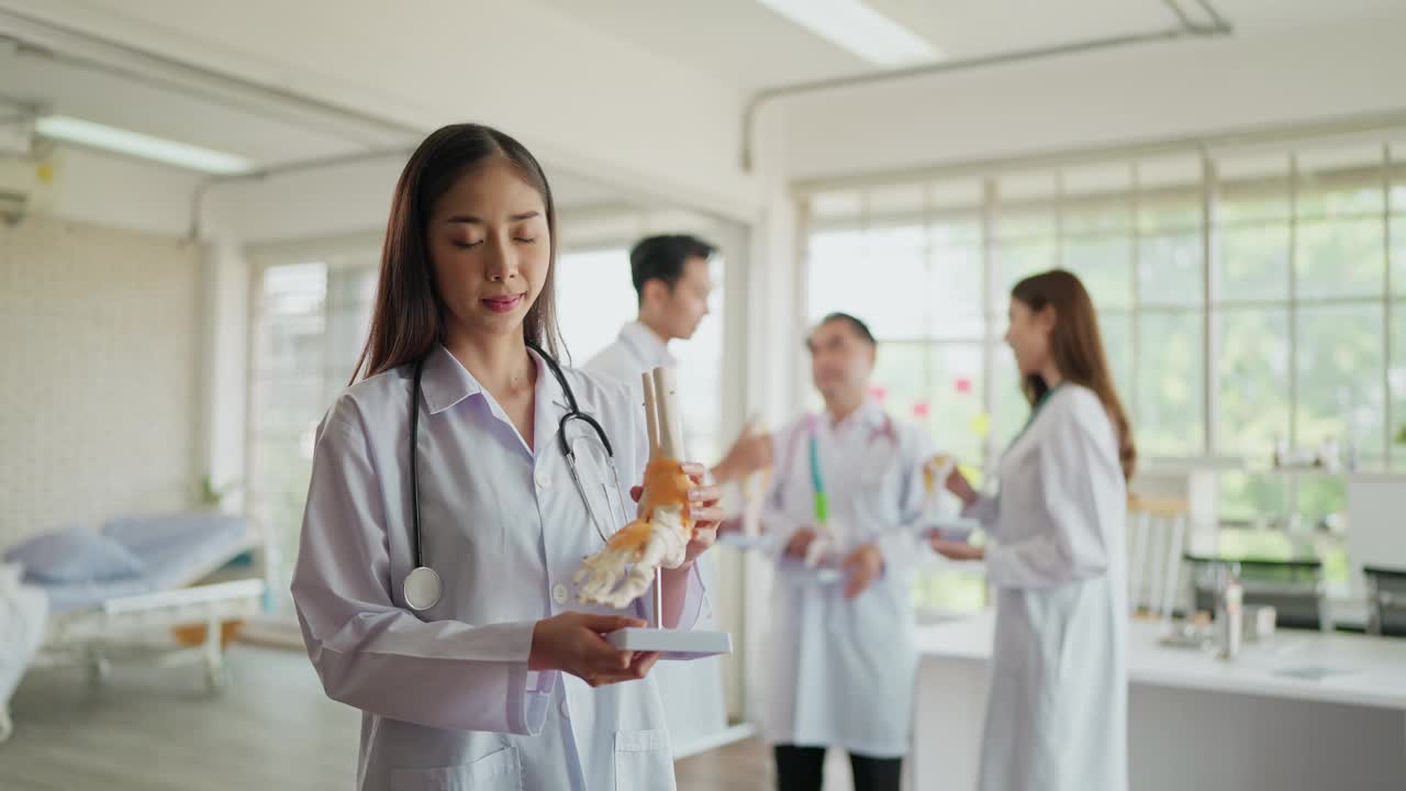 穿着制服的年轻亚洲女性骨科医生的肖像，抱着人体踝关节骨骼模型，在医院对着镜头微笑。医疗整形外科医师