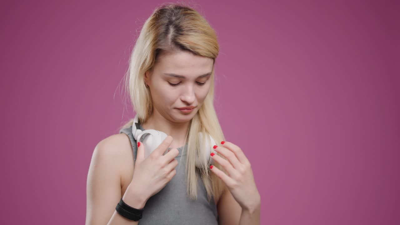 年轻的金发女子通过白色耳机在粉红色的背景下欣赏音乐