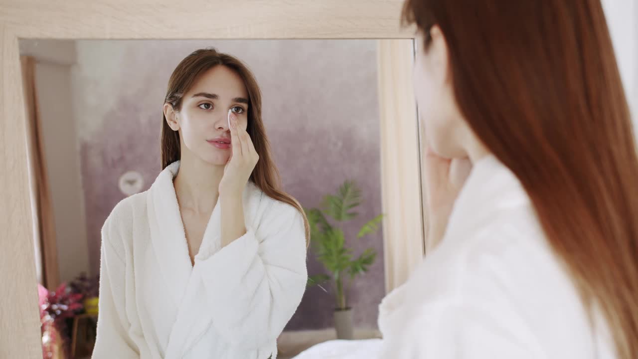 穿着白色浴袍的漂亮女人看着家里的大镜子