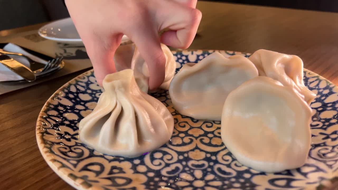 用手把螳螂放在盘子里。妇女拿着传统的格鲁吉亚饺子，Khinkali，用叉子，近距离观察双手。