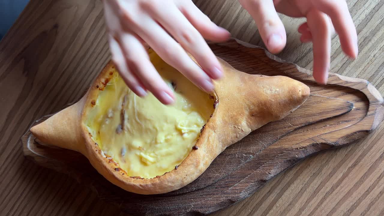 阿贾利安语的khachhapuri，装在木盘上。女孩掰开一块美味的食物——格鲁吉亚菜，一种民族面粉制品，一种填有奶酪和鸡蛋的馅饼。
