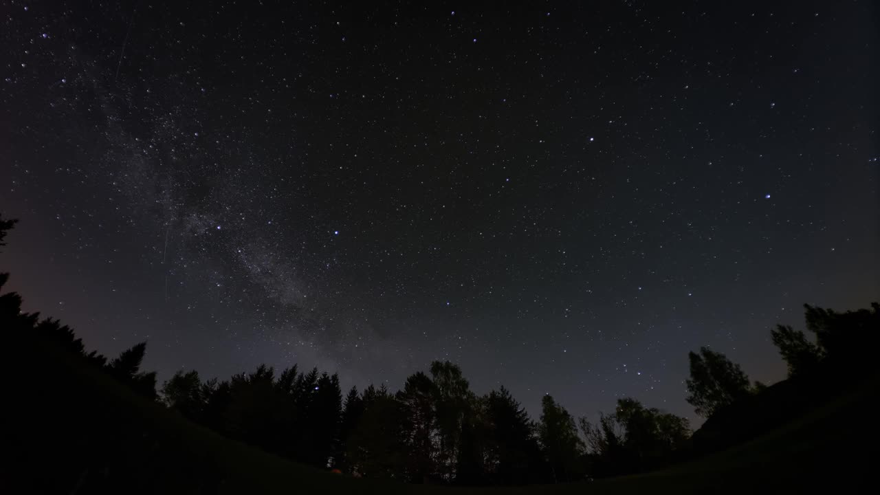 时间流逝的恒星，包括银河系，在剪影森林上方移动。还有卫星和流星划过天空。