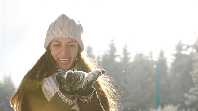 迷人的年轻女子吹雪花在照相机太阳耀斑