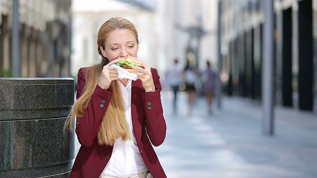 快午餐，忙碌的女人。一个年轻的女人在城市的街道上吃汉堡包。