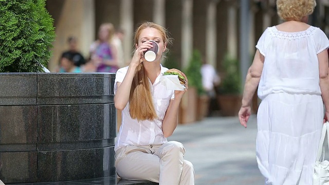 快午餐，忙碌的女人。一个年轻的女人在城市的街道上吃汉堡包。