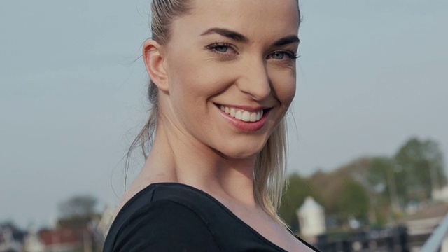 美丽的年轻女子站在桥上对着镜头微笑，在户外。