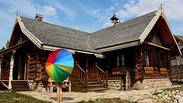 酒吧里的女孩在一间乡村小屋旁挥动着五颜六色的雨伞