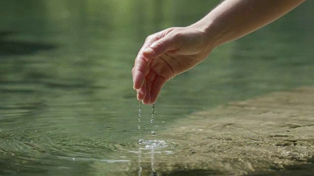 慢镜头特写:手握着，把新鲜的水倒进美丽的山泉湖中