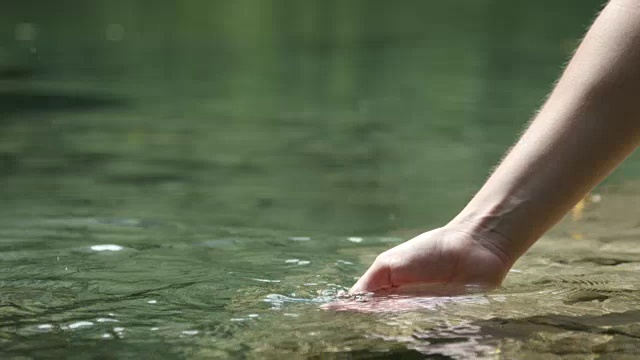 慢镜头近景:用手在美丽的山湖中玩清澈的水