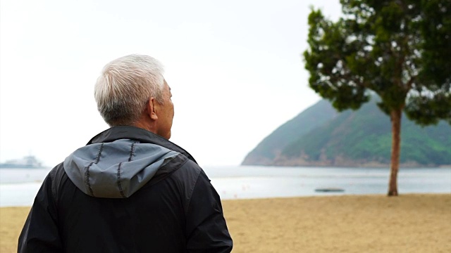 一个亚洲老人独自站在海滩前