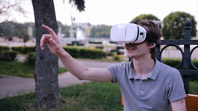 详情图-年轻人戴着3D,VR头戴显示器在公园里观看360度电影,玩VR游戏