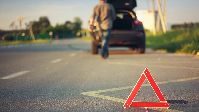 道路上的红色三角形警告，汽车抛锚，司机在后备箱里找工具