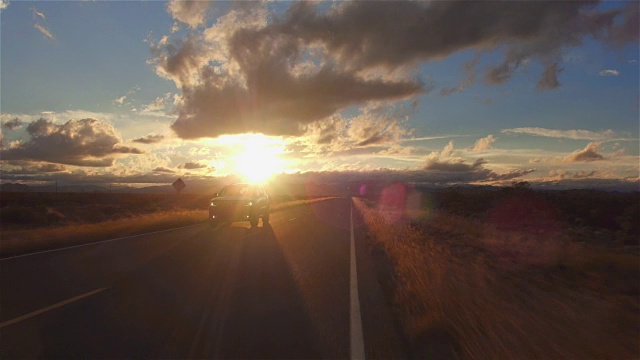 图片:金色的夕阳下，一辆黑色SUV行驶在空旷的乡村道路上