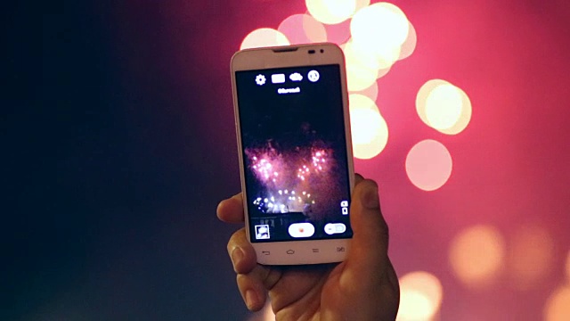 无法识别的手与智能手机拍摄和拍照的烟花表演。美丽的烟花高清