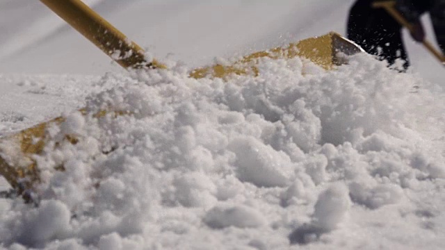 在滑雪胜地，人们用铁铲清除积雪。阳光明媚的一天。山。喷洒。雪堆